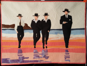 Art Quilt showing four figures walking across a wet sandy beach.