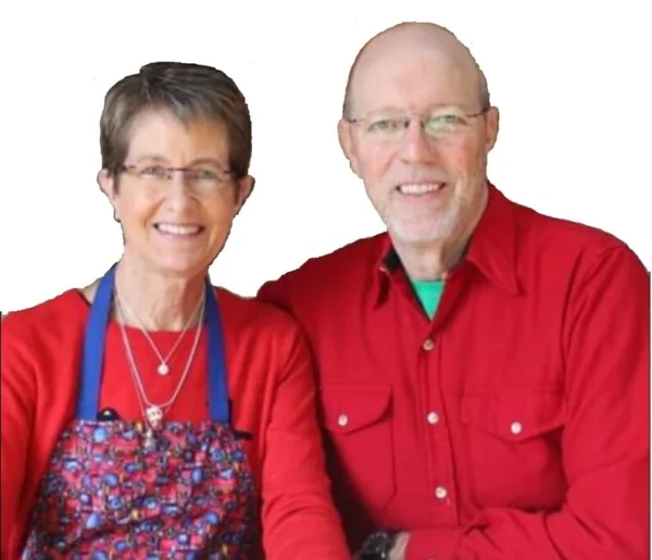 Two people sitting together, both wearing red shirts. The Woman is wearing a blue apron with a colorful pattern.