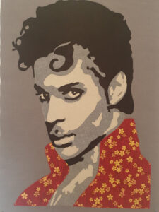 An Art Quilt of a male singer with curly black hair and a flowered shirt.