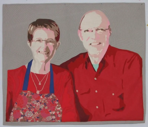 The image is of a fabric Art Quilt depicting a woman and a man dressed in red, sitting side by side.